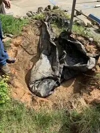 Image 2: After digging out the soil and other debris from the bottom of the pond, the liner was gathered up to in preparation to be removed.