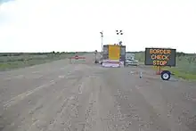 an electronic sign that says "Border Check Stop" on a gravel road.