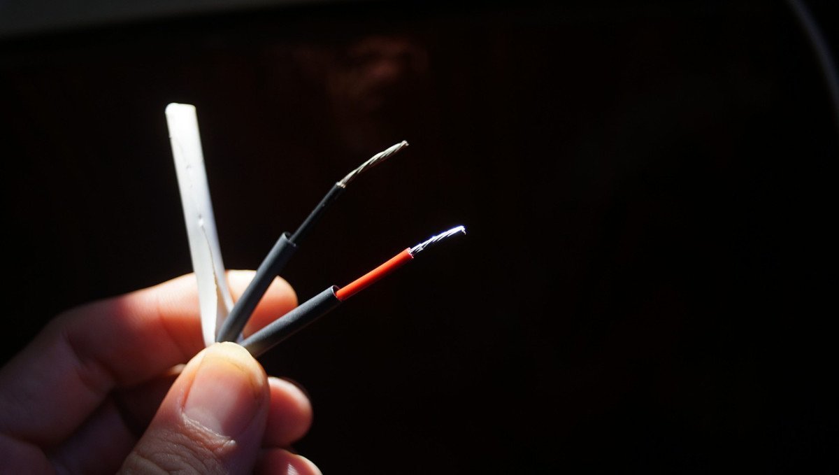 photo of a hand holding two wires, a positive and a negative