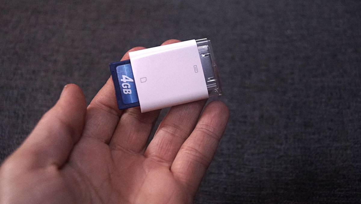 a hand is holding a 30-Pin Male to SD card camera connector, with an SC card inserted