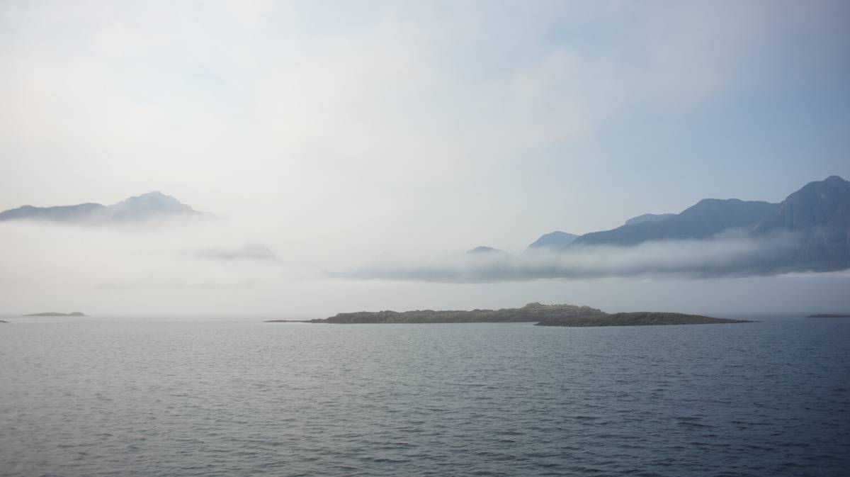 anchored in boat bay in johnstone strait, a reef is visible, with fog covering far away mountains