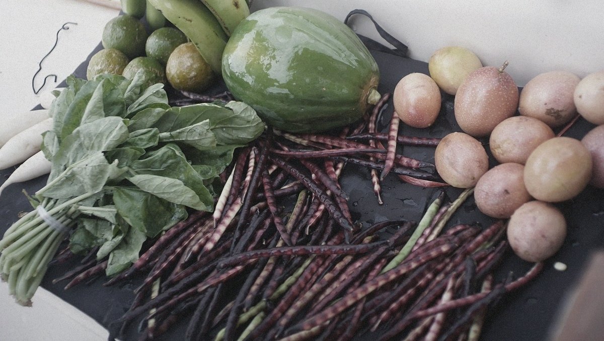 A photo of fresh produce, papaya, long beans, passion fruit, limes and greens, drying outside