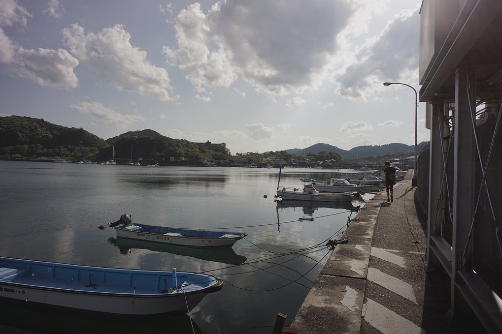 Devine walking along the Gokasho fishing harbor, with small boats moored onto it