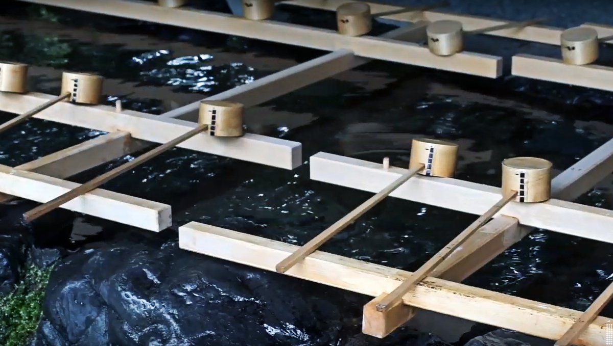 a photo of a Temizusha, a series of wooden ladles sit over a basin of fresh water