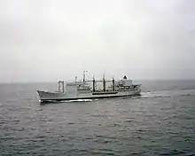 A grey ship. It has three large refuelling booms midship, with black hoses.