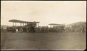 Two biplanes in a field surrounded by a crowd