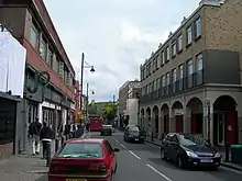 Photograph of a busy street with cars and pedestrians, with buildings on both sides