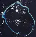 A 2002 true-color photograph of Enewetak Atoll. The relatively large Ivy Mike crater can be seen at the top of the atoll in this image with the smaller, adjoining Castle Nectar crater, in close proximity. The much smaller Redwing Seminole crater can faintly be seen on Bogon Island.