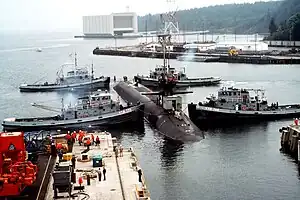 Naval Submarine Base Bangor with tug Mishawaka (rear left) and three other Natick-class tugs guiding the USS Ohio (SSGN-726) out of dry dock at Delta Pier