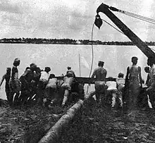 GIs and Indian laborers launch a pontoon on the Hooghly River.  Two pontoons lashed together will float pipe to the opposite bank.  The main portion of the pipeline will then lie along the river's bottom.