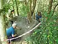 Staff and volunteers smoothing surface of mud sofa, a temporary barrier of local material