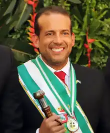Headshot of Luis Fernando Camacho adorned in gubernatorial regalia and holding a baton.