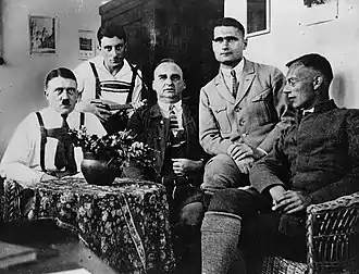 Black-and-white photo of five men sat at a table, with Maurice holding a musical instrument