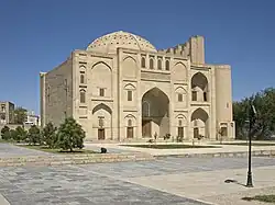 A brick building with a large portal and a dome, surrounded by trees and a pond