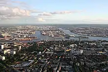 A color photograph showing an aerial view of a city. The bottom of the photograph shows more of the city's buildings and houses, while towards the center and upward is the city's waterways.