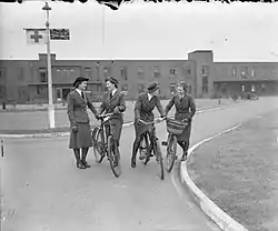 A black and white image of four nursing sisters on pushbikes outside a hospital block