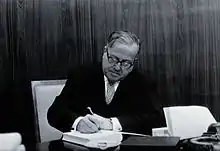 Rudolf Geigy, seated at a table, signing a book