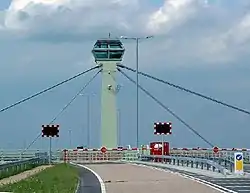 A cable-stayed tower with barriers and flashing lights on the road deck beneath