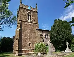 Church of St Martin with its tower and blue clock face surrounded by its grass-covered graveyard