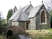 A small stone church seen from the southeast with a short chancel, a porch at the southeast, a buttressed nave, and a west bellcote