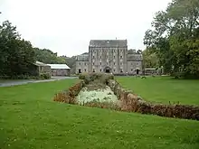 canal-type waterway running through a meadow to a large grey four-storey building in the distance
