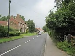 A rural street with house on the left, and hedges and trees on the right