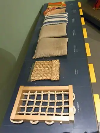 Touchable museum samples illustrating the layers of the Great Bed of Ware: the bedcords, a plaited-rush bedmat, a flockbed and then a featherbed in dun ticking, a downbed in striped ticking, and the bedlinen. Flock is unspun fibers, in this case probably wool. The bedticks stuffed with the softest fillings are laid topmost.
